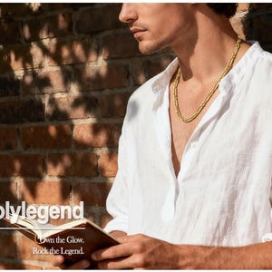 May include: A gold-colored necklace worn over a white linen shirt. The image shows a person holding a small brown book with the text "Holylegend" and the tagline "Own the Glow. Rock the Legend."