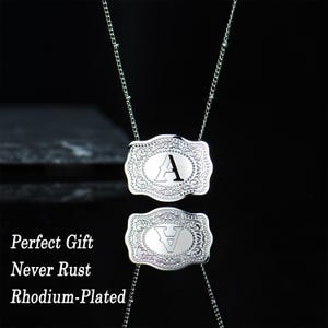 May include: A silver necklace with two rectangular pendants featuring the letter "A" in a decorative font. The pendants have a detailed, ornate design.