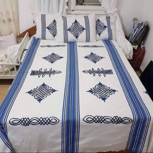 May include: White bed linens with blue geometric patterns and stripes. The set includes a fitted sheet, a flat sheet, and pillowcases. The design features a repeating pattern of diamond shapes and linear accents, creating a cohesive look.