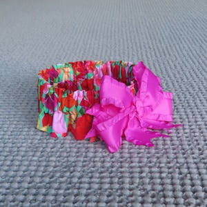 May include: A floral print headband with a large, bright pink bow. The headband is made of fabric and has a gathered elastic band.