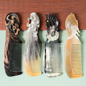 May include: Four decorative combs with animal-themed designs. The combs feature intricate carvings of a bird, a fish, and other creatures. The combs are made of dark and light-colored materials, with detailed patterns and textures. The combs are displayed against a neutral background.