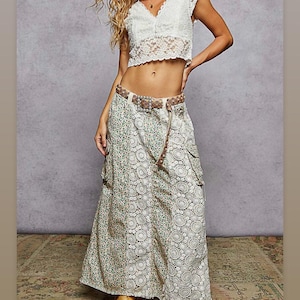 May include: A white lace crop top and a long skirt with a floral and circular pattern. The skirt has two pockets and is paired with a brown belt. The outfit is completed with tan boots. The overall style is bohemian.