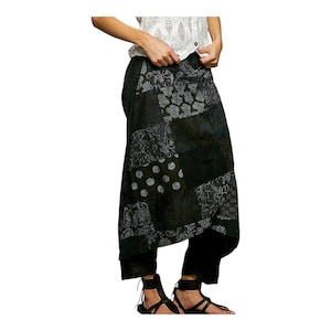 Puede incluir: Falda negra de patchwork con varios diseños florales y geométricos en blanco. La falda se combina con pantalones negros y sandalias. La parte superior es un suéter blanco de punto abierto. La falda tiene un diseño asimétrico único.