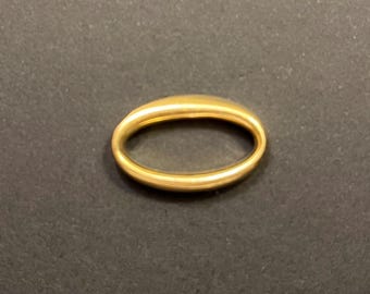 May include: A gold-colored ring with an oval shape. The ring is smooth and appears to be made of metal. The ring is set against a dark background. Jewelry.