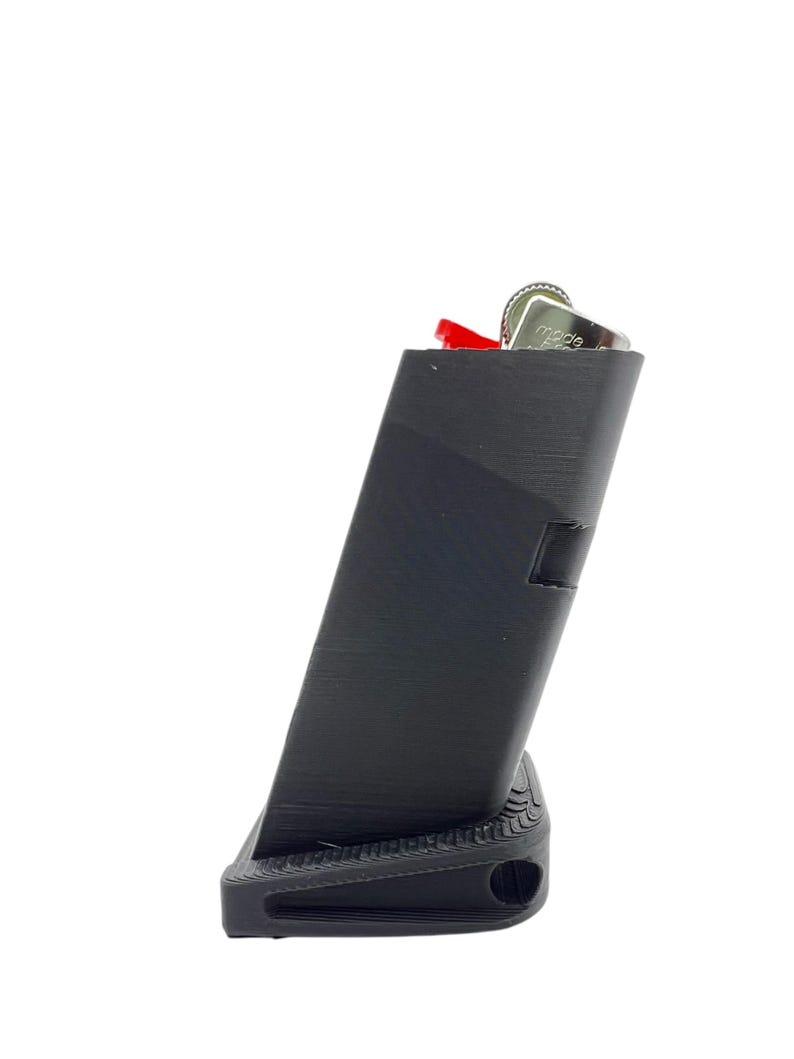 May include: A black plastic magazine holder with a red lighter inside. The holder has a textured surface and a small hole on the bottom.