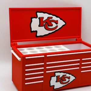 May include: Red toolbox-style cooler with white accents and the Kansas City Chiefs logo. The cooler has a hinged lid and a white interior with circular compartments. The exterior features the team logo and white horizontal stripes.