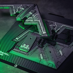May include: A detailed model of a B-2 Spirit stealth bomber, featuring a gray and black color scheme with green accent lighting. The model is displayed on a textured surface with the "Bambu Lab" logo and "B-2 SPIRIT" text.