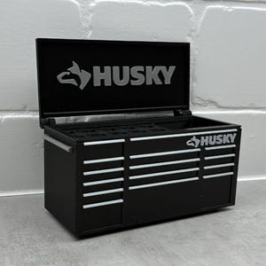 May include: Black tool chest with the word "HUSKY" in silver lettering on the front and lid. The chest has multiple drawers with silver handles.