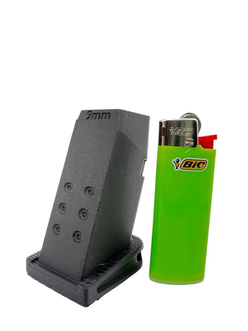 May include: A black 9mm magazine extension for a pistol, next to a green Bic lighter for size comparison.