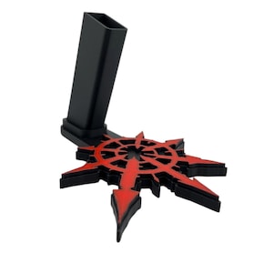 Puede incluir: Un soporte de plástico negro con un diseño de estrella roja y negra. El soporte está diseñado para sostener un teléfono u otro dispositivo.