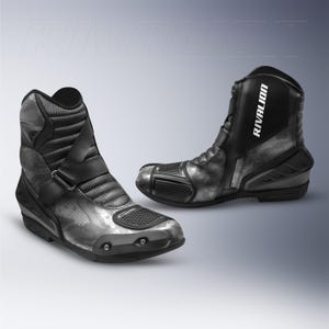 Puede incluir: Par de botas de moto negras y grises con la palabra "RIVALION" impresa en el lateral. Las botas tienen un patrón de camuflaje, un cierre de hebilla y una zona de puntera reforzada. Diseñadas para protección y estilo.