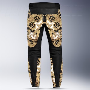 May include: Black motorcycle pants with a gold baroque pattern on a white background. The pants have black panels on the sides and knees. The waist area is black and ribbed.