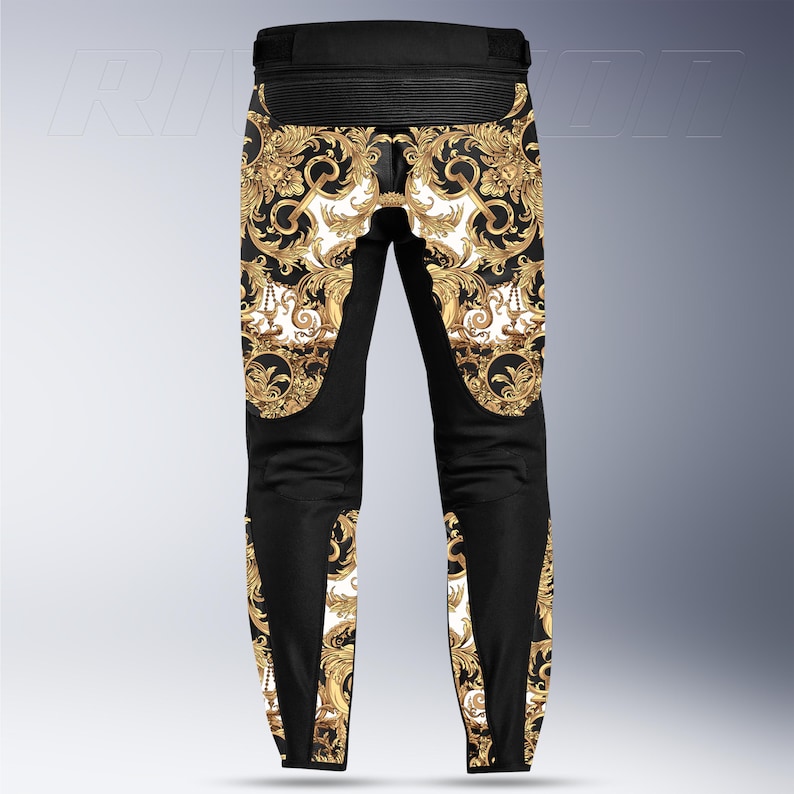May include: Black motorcycle pants with a gold baroque pattern on a white background. The pants have black panels on the sides and knees. The waist area is black and ribbed.