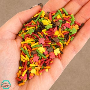 Puede incluir: Una colección de virutas decorativas para repostería con temática otoñal en colores rojo, naranja, amarillo, verde y marrón. El surtido incluye palitos y pequeñas piezas de azúcar con forma de hoja, con el logotipo de Simply Sucré visible.