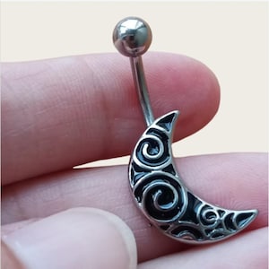 May include: A silver belly button ring featuring a crescent moon design. The moon is black with a swirling pattern. The top ball is silver and the post is straight.