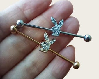 May include: Two industrial barbells. One is silver, the other is gold. Each barbell has a small, sparkling bunny charm and a ball at each end. The bunny charms are encrusted with small, clear crystals.