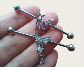 May include: Two silver-toned industrial barbells, each with a butterfly charm. One butterfly has a pink centre stone, the other has clear stones with a dangling design. Each barbell has a ball at either end.