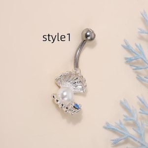 May include: Silver belly button ring with a pearl in a shell charm. The shell is open and has a blue rhinestone on the bottom. The ring is labelled "style1".