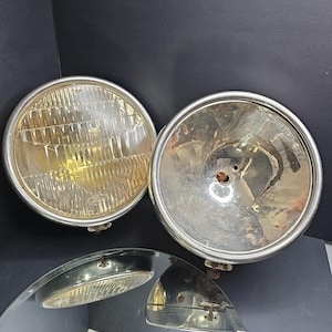 May include: Two vintage car headlights with chrome rims. One headlight has a clear, ribbed lens, while the other is a chrome reflector. The third piece is a headlight lens. These classic auto parts are likely from an older vehicle.
