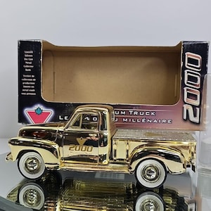 May include: A gold-colored die-cast metal Millennium Truck model with white-walled tires. The truck is in its original box, which has text in English and French. The model truck has the number "2000" on the side.