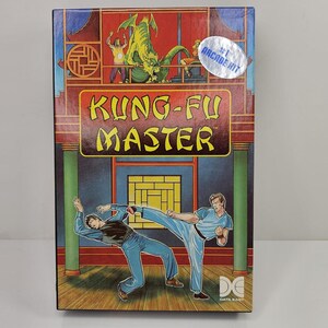 Peut inclure: Une boîte de jeu vidéo rectangulaire pour Kung-Fu Master présentant une illustration colorée de deux personnages se battant dans un temple. Un dragon vert est visible en haut et un autocollant argenté indique #1 ARCADE HIT. Le logo Data East est en bas.