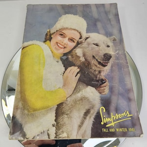 May include: Vintage magazine cover featuring a woman in a yellow sweater and white fur-trimmed vest, embracing a large white dog. The cover has the text "Simpson's Fall and Winter 1941" in yellow script.