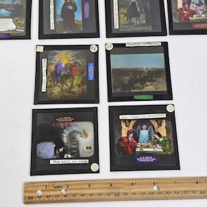 May include: A collection of vintage slides, each in a black frame, depicting historical and religious scenes. Text on the slides includes "Flight into Egypt" and "The Game in progress". A wooden ruler, marked in inches, is at the bottom.