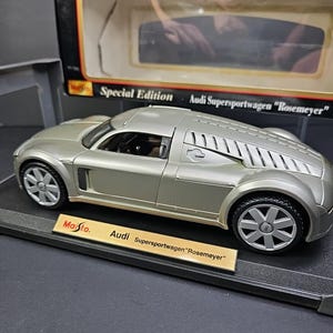 May include: A silver Audi Supersportwagen "Rosemeyer" model car. The diecast model features detailed wheels, a sleek body design, and the text "Maisto" and "Special Edition" on the packaging. The model is displayed on a black base.