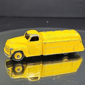 May include: A classic yellow toy truck with black wheels and a rounded tank. The truck shows signs of age and use. The words "Benzol Motor" are printed on the side of the tank.