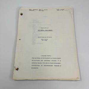 May include: A vintage script for the TV show "QUINCY", episode "HOT ROCKS, COLD HEARTS". The document is cream-coloured with black text, featuring production details and a copyright notice. It has three-hole punch binding.