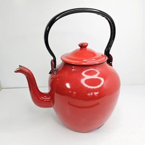 May include: A red enamel teapot with a black handle and spout. The teapot has a round body and a lid. The handle is arched, and the spout is curved. A classic design for making tea.
