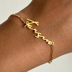 Könnte beinhalten: Ein goldenes Kettenarmband mit einem personalisierten Namensschild, auf dem "Karisma" steht.