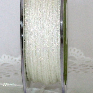 May include: A spool of white, sparkly ribbon. The ribbon is tightly wound on a clear plastic spool with silver edges. The ribbon has a shimmering, iridescent quality, catching the light. A few strands of ribbon are loose at the bottom.
