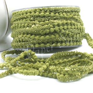 May include: A spool of olive green pom-pom trim with a decorative edge. The trim is made of small, round pom-poms and a gold-colored thread. The trim is on a white surface.