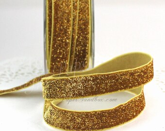 May include: Gold glitter ribbon, displayed in a glass container and coiled. The ribbon has a soft, velvety texture and is covered in sparkling gold glitter. The ribbon is approximately 0.5 inches wide, perfect for crafts and decorations.