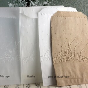 Op de afbeelding: Vier papieren zakken in wit, glassine en kraftpapier. Elke zak heeft een reli&euml;fontwerp van een dorpsgezicht met bomen en stippen. De tekst "White paper", "Glassine" en "White and Kraft Paper" is op de zakken gedrukt.