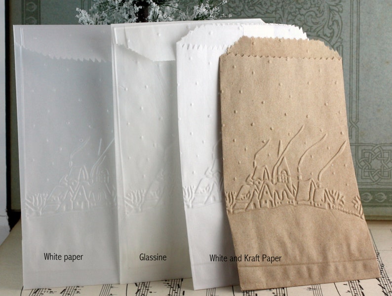 Op de afbeelding: Vier papieren zakken in wit, glassine en kraftpapier. Elke zak heeft een reli&euml;fontwerp van een dorpsgezicht met bomen en stippen. De tekst "White paper", "Glassine" en "White and Kraft Paper" is op de zakken gedrukt.
