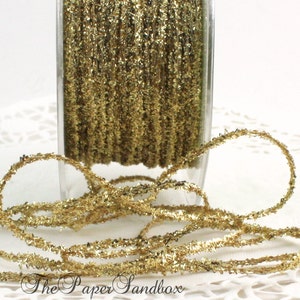 May include: Gold metallic ribbon in a clear glass container. The ribbon is a continuous strand of small, shiny, gold-colored pieces. The Paper Sandbox logo is visible at the bottom.