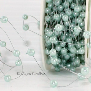 May include: A spool of light blue pearl beads on a silver wire. The beads are round and evenly spaced, creating a delicate and elegant look. The PaperSandbox logo is visible in the bottom left corner. Ideal for crafting and decorative projects.