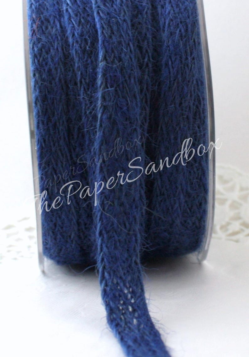 Op de afbeelding: Een spoel marineblauw gevlochten jute touw. Het touw is strak opgerold en heeft een textuur. De spoel is gedeeltelijk zichtbaar, met de tekst "PaperSandbox" in een scriptlettertype.