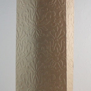 May include: A tall, rectangular paper bag with a damask pattern embossed on the surface. The bag is beige and has a scalloped top edge. The word "Damask" is printed at the bottom.