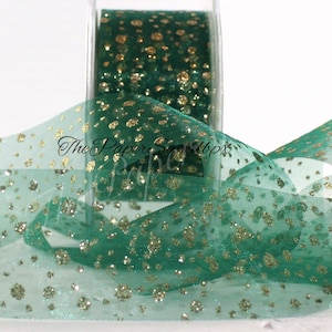 May include: A spool of emerald green sheer ribbon with gold glitter dots. The ribbon is partially unrolled, displaying its delicate texture and sparkle. The text "The Paper Scraps Babe" is visible on the ribbon.