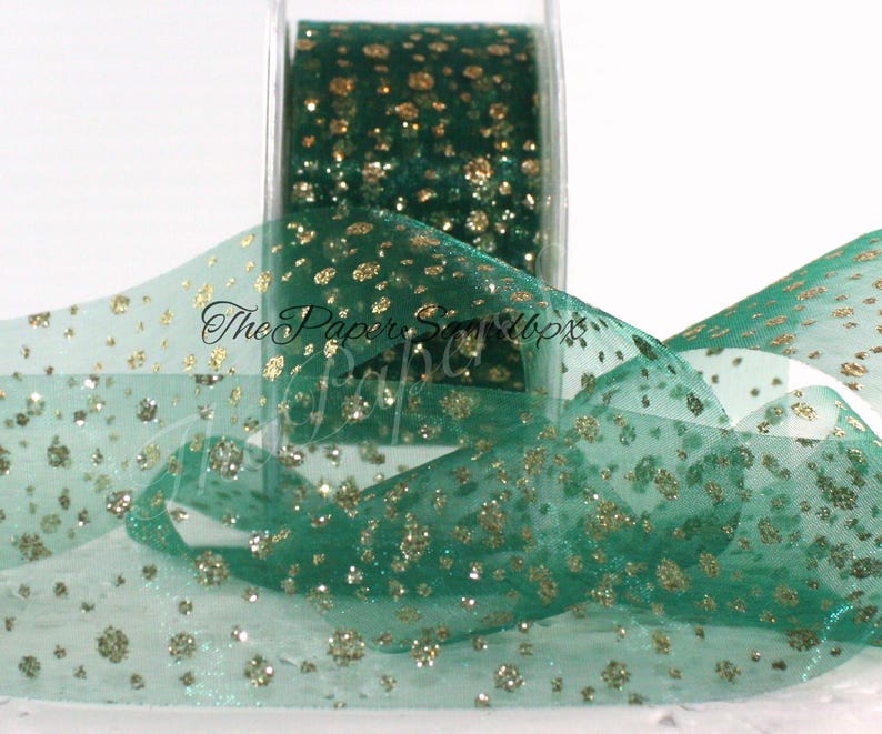 May include: A spool of emerald green sheer ribbon with gold glitter dots. The ribbon is partially unrolled, displaying its delicate texture and sparkle. The text "The Paper Scraps Babe" is visible on the ribbon.