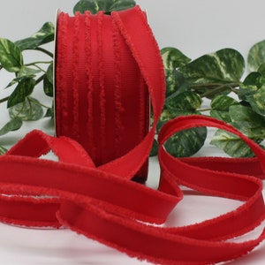 May include: A spool of bright red ribbon with a textured, frayed edge. The ribbon is displayed against a backdrop of green foliage, highlighting its vibrant color and decorative potential. The ribbon is ideal for crafts and gift wrapping.