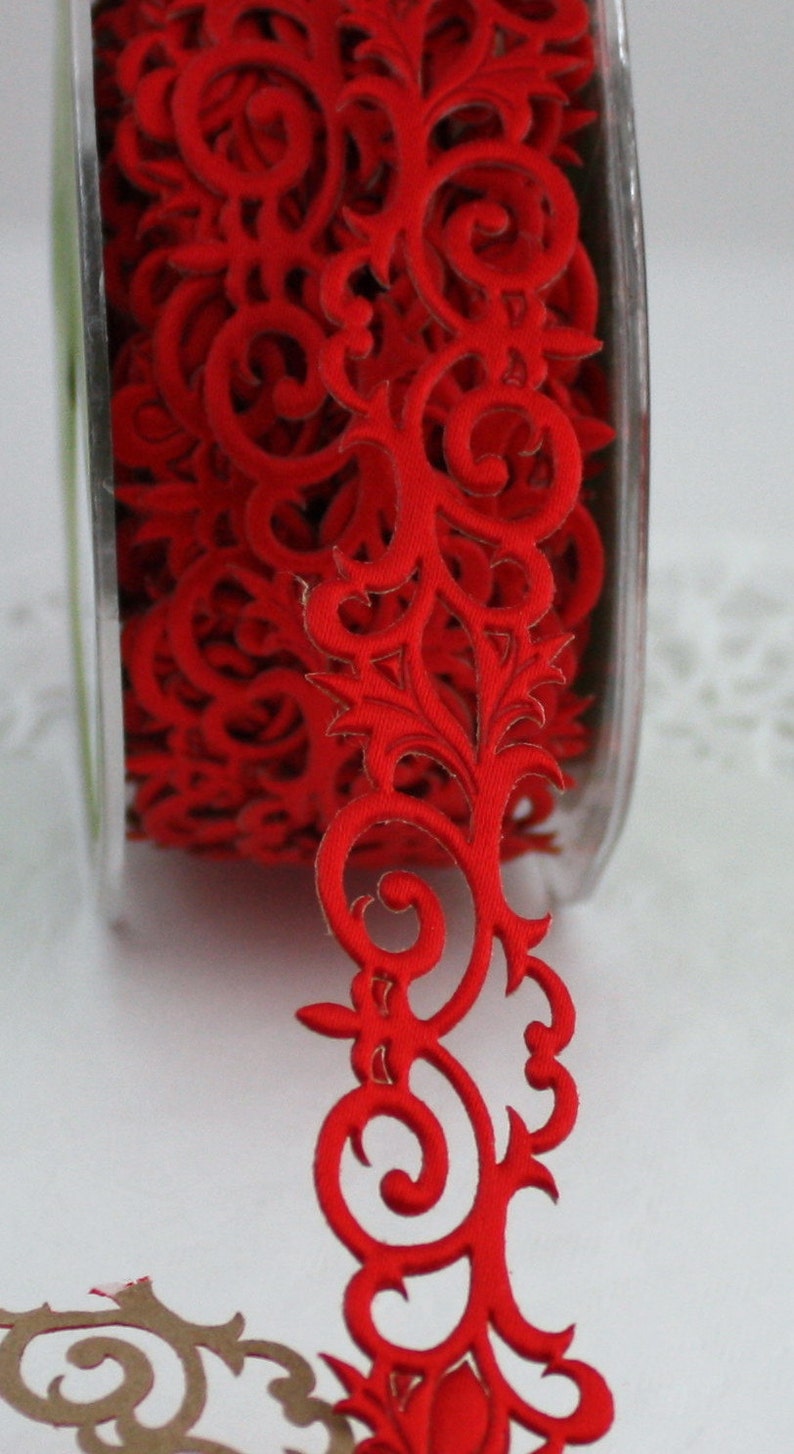 May include: A spool of red decorative ribbon with a repeating floral scroll design. The ribbon is made of a soft fabric and is ideal for crafts, gift wrapping, or embellishing various projects. The ribbon is on a clear plastic spool.