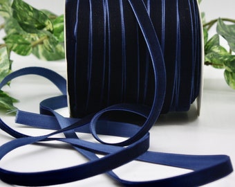May include: A spool of navy blue velvet ribbon. The ribbon is a deep, rich blue color and has a soft, velvety texture. The ribbon is unrolled, with a length of the ribbon lying flat in the foreground.