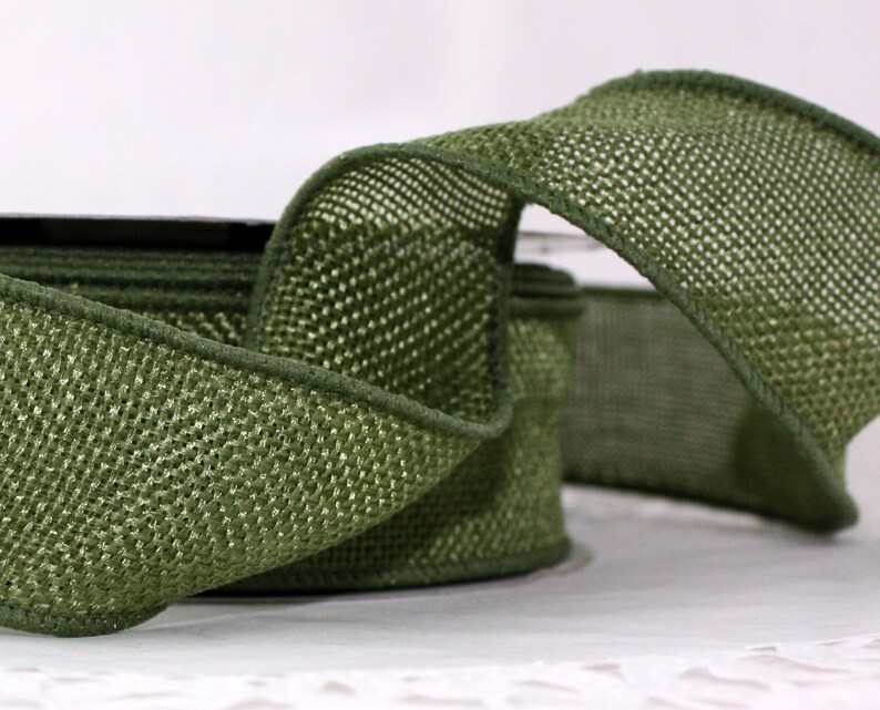 May include: Close-up of a roll of olive green ribbon. The ribbon has a woven texture and a darker green trim along the edges. The ribbon is partially unrolled, revealing the texture and color.
