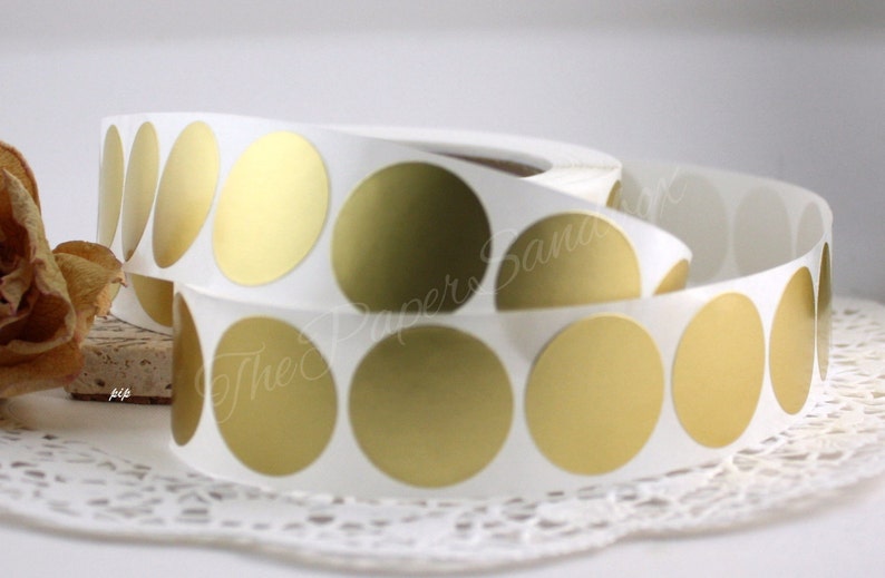 May include: Rolls of white sticker paper with gold metallic circle stickers. The stickers are arranged in a continuous roll, with a few stickers peeled away. The Paper Sandbox is printed on the sticker roll.