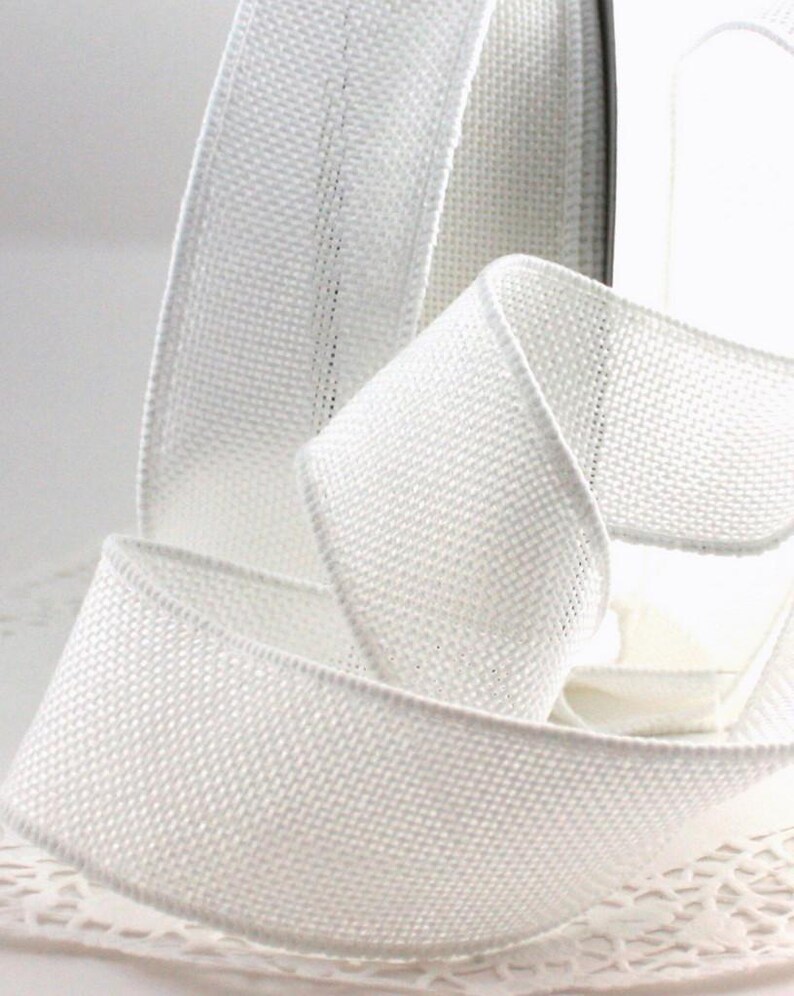 May include: A roll of white ribbon with a woven texture. The ribbon is curled and folded, showcasing its flexibility and form. The edges are neatly finished, and the ribbon appears to be made of a sturdy material, suitable for various crafting projects.