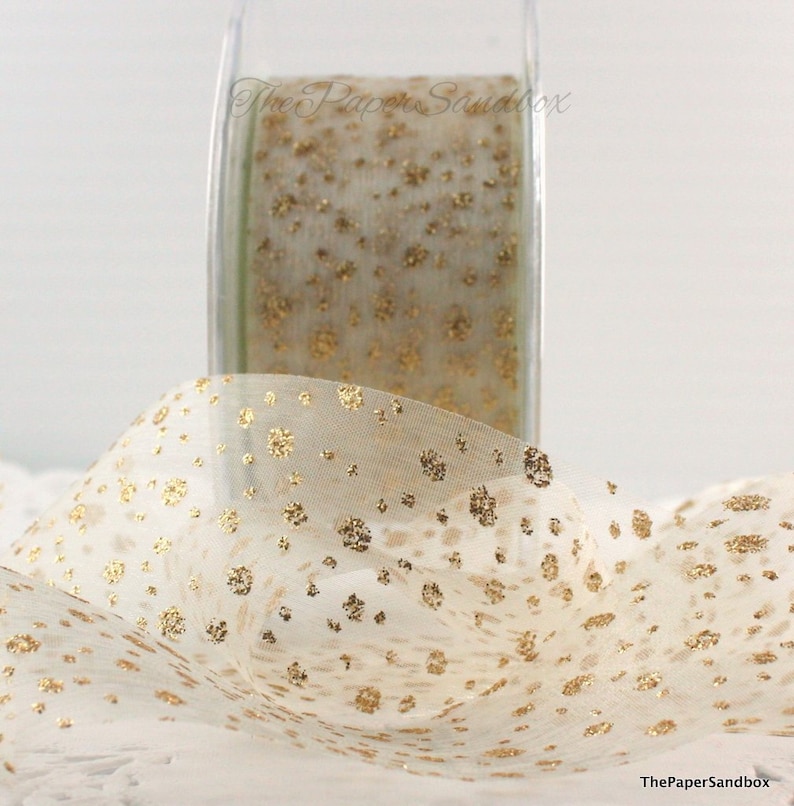 May include: A roll of sheer ivory ribbon with gold glitter floral accents. The ribbon is partially unrolled, revealing the delicate pattern. The Paper Sandbox is printed on the roll and in the lower right corner.